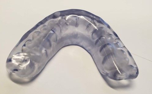 A clear mouth guard is sitting on a white surface.