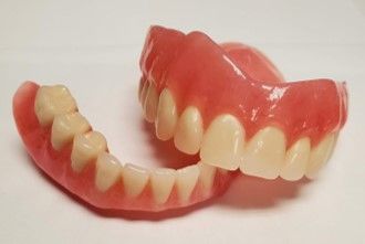 A pair of dentures sitting on top of each other on a white surface.