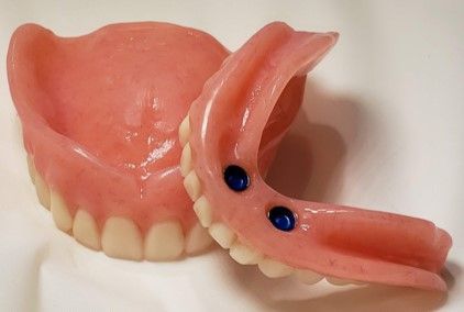 A pair of dentures with blue buttons on them are sitting on a white surface.