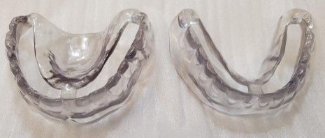 Two clear plastic mouth guards are sitting on a white surface.