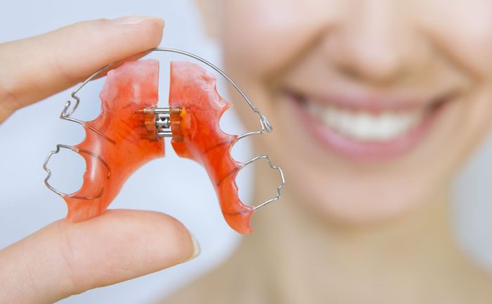 A woman is holding a red retainer in her hand.