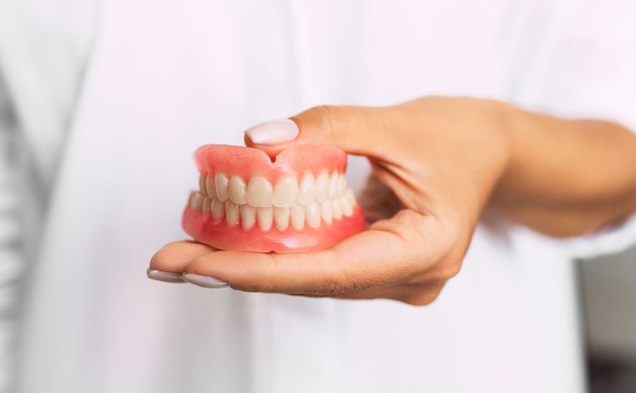 A woman is holding a model of dentures in her hand.
