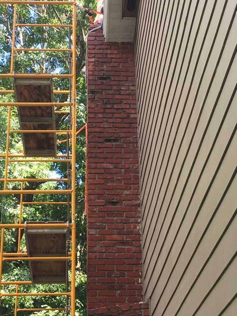 A brick chimney is being repaired on the side of a house