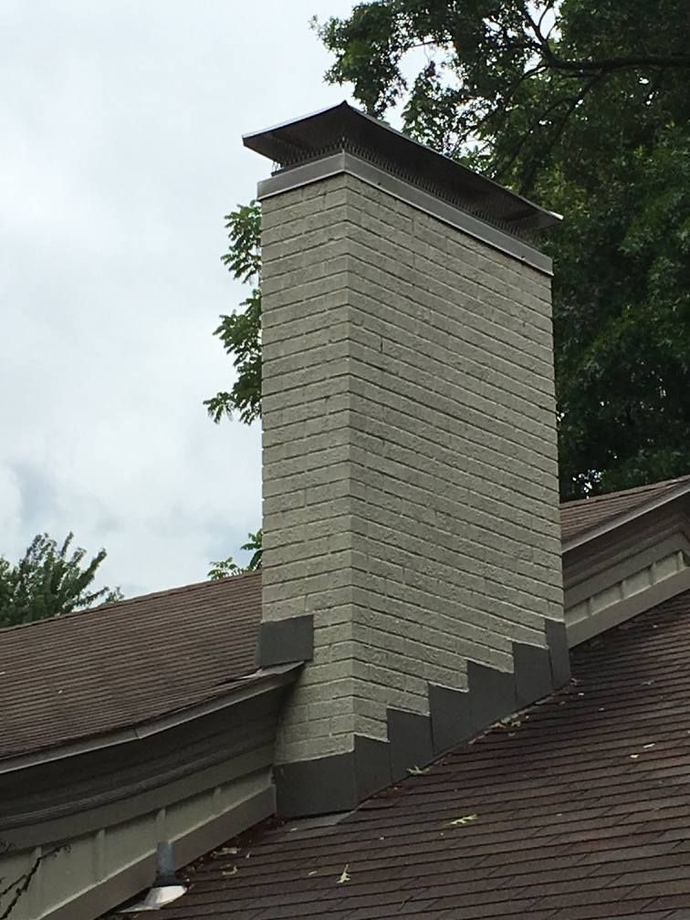 A brick chimney is sitting on top of a brown roof.