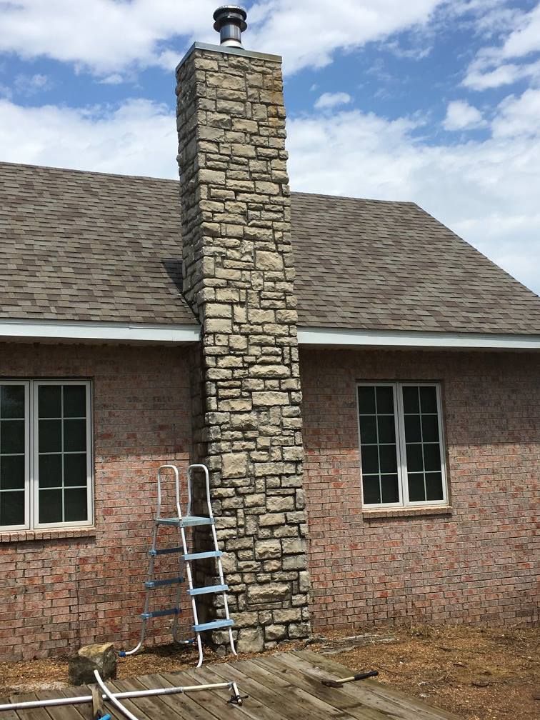 A large stone chimney on the side of a brick house