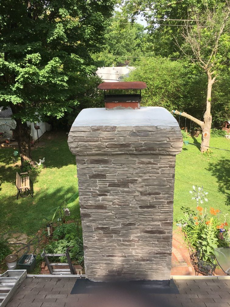 A chimney is sitting on top of a brick wall in a backyard.