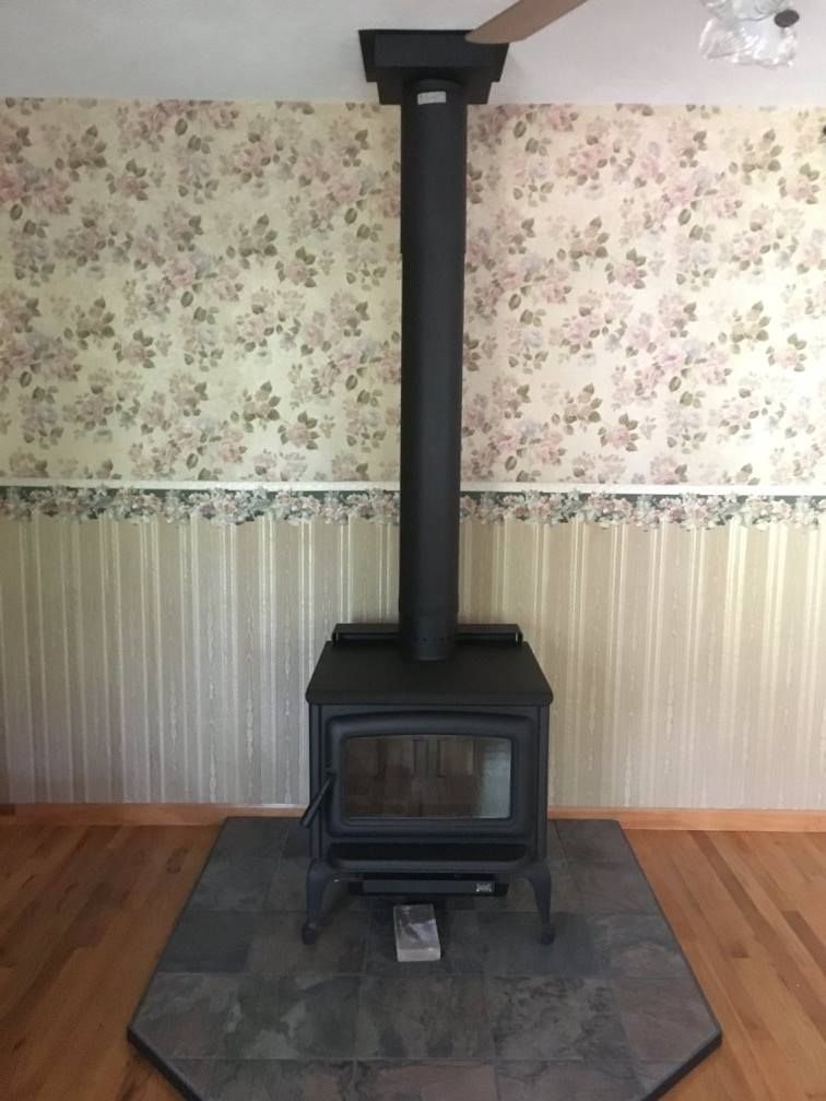 A wood stove in a living room with floral wallpaper