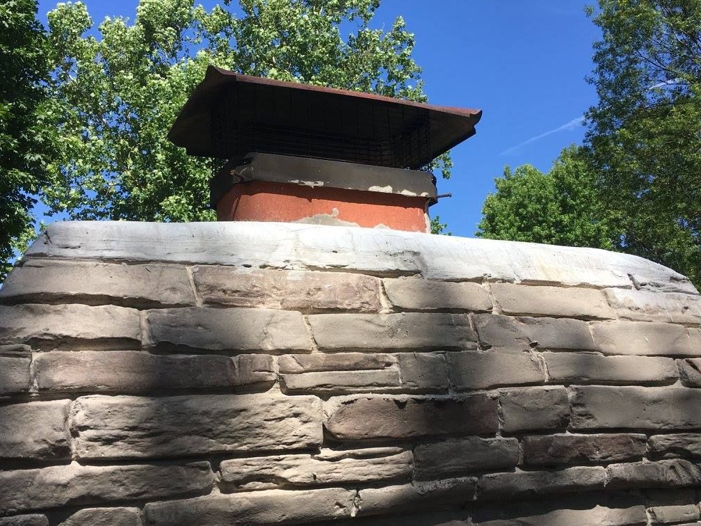 A chimney on top of a stone wall with trees in the background