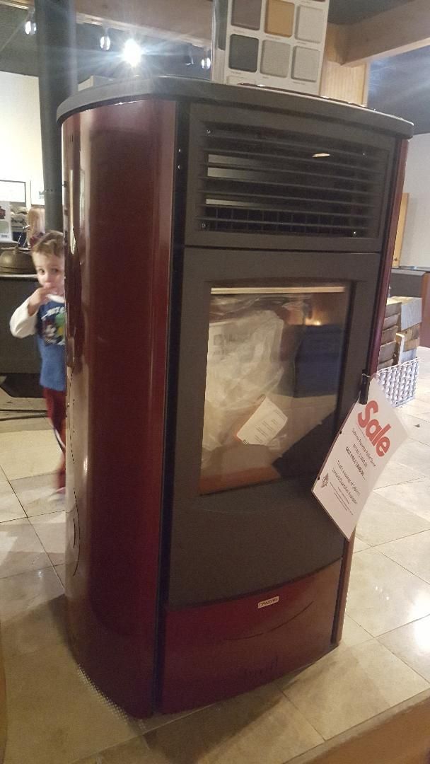 A little boy is standing next to a red stove in a room.