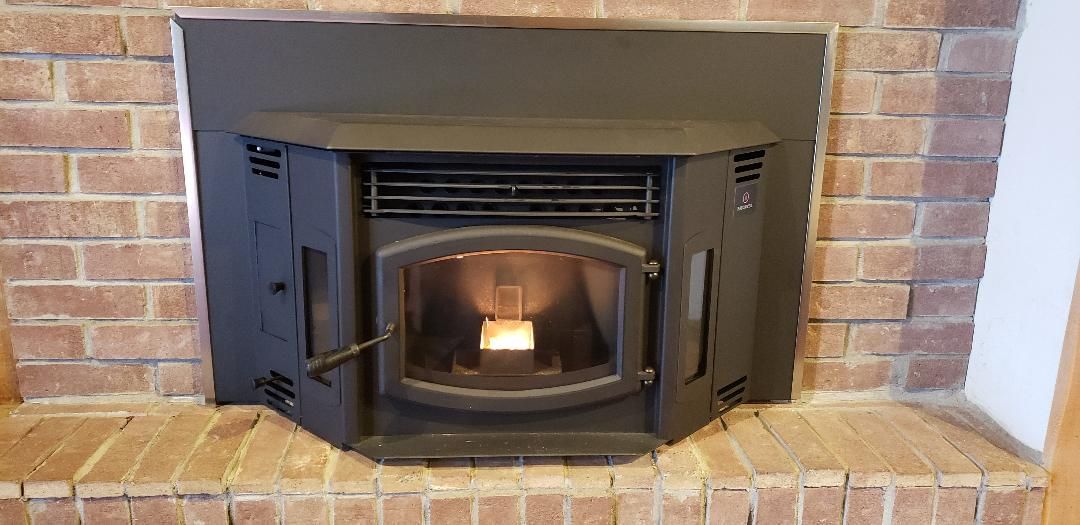 A wood stove is built into a brick fireplace.