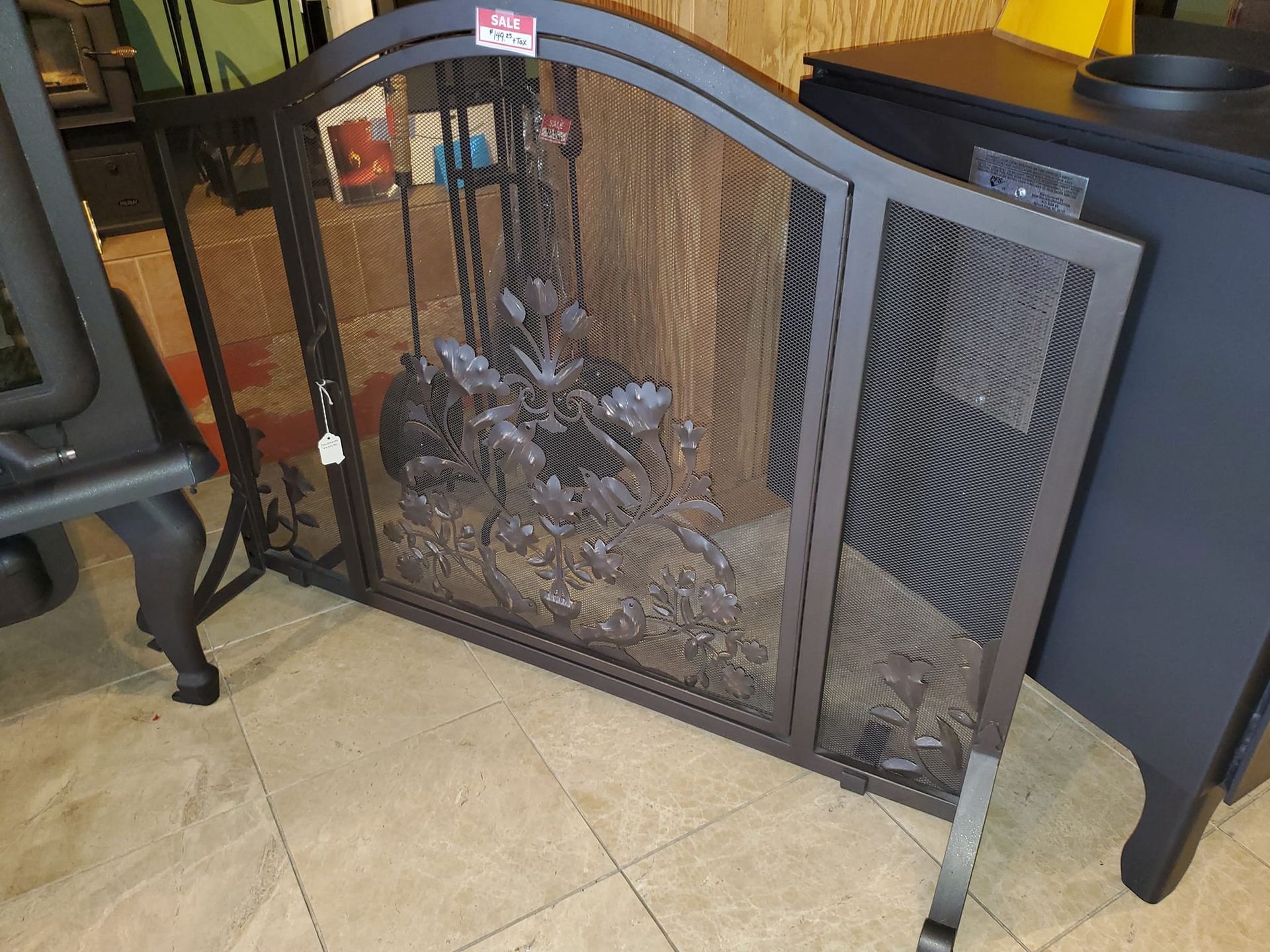 A fireplace screen is sitting on a tiled floor in front of a fireplace.