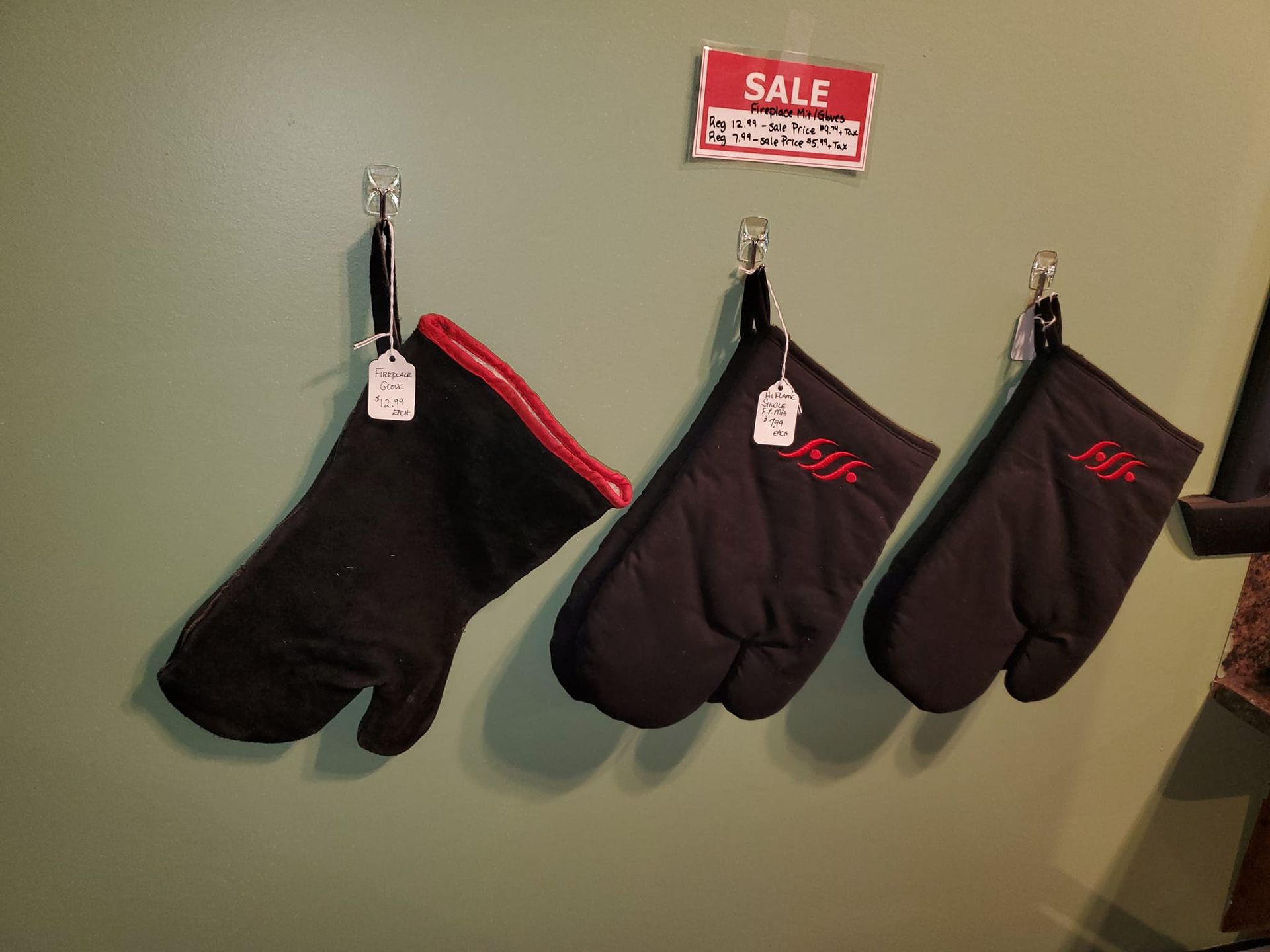 Four black oven mitts are hanging on hooks under a sale sign