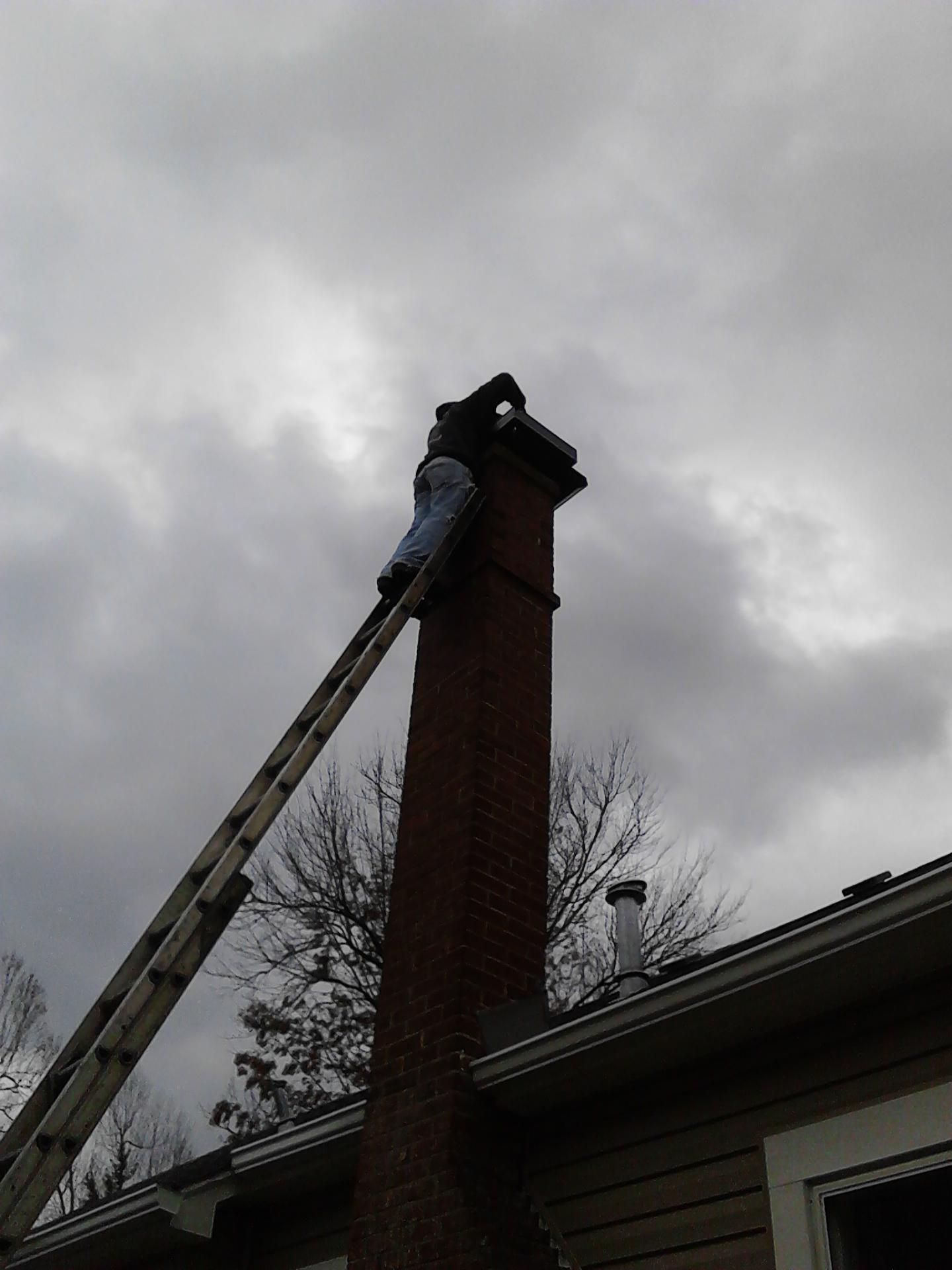 A man is standing on a ladder next to a chimney.