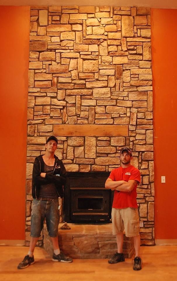 Two men are standing in front of a stone fireplace.