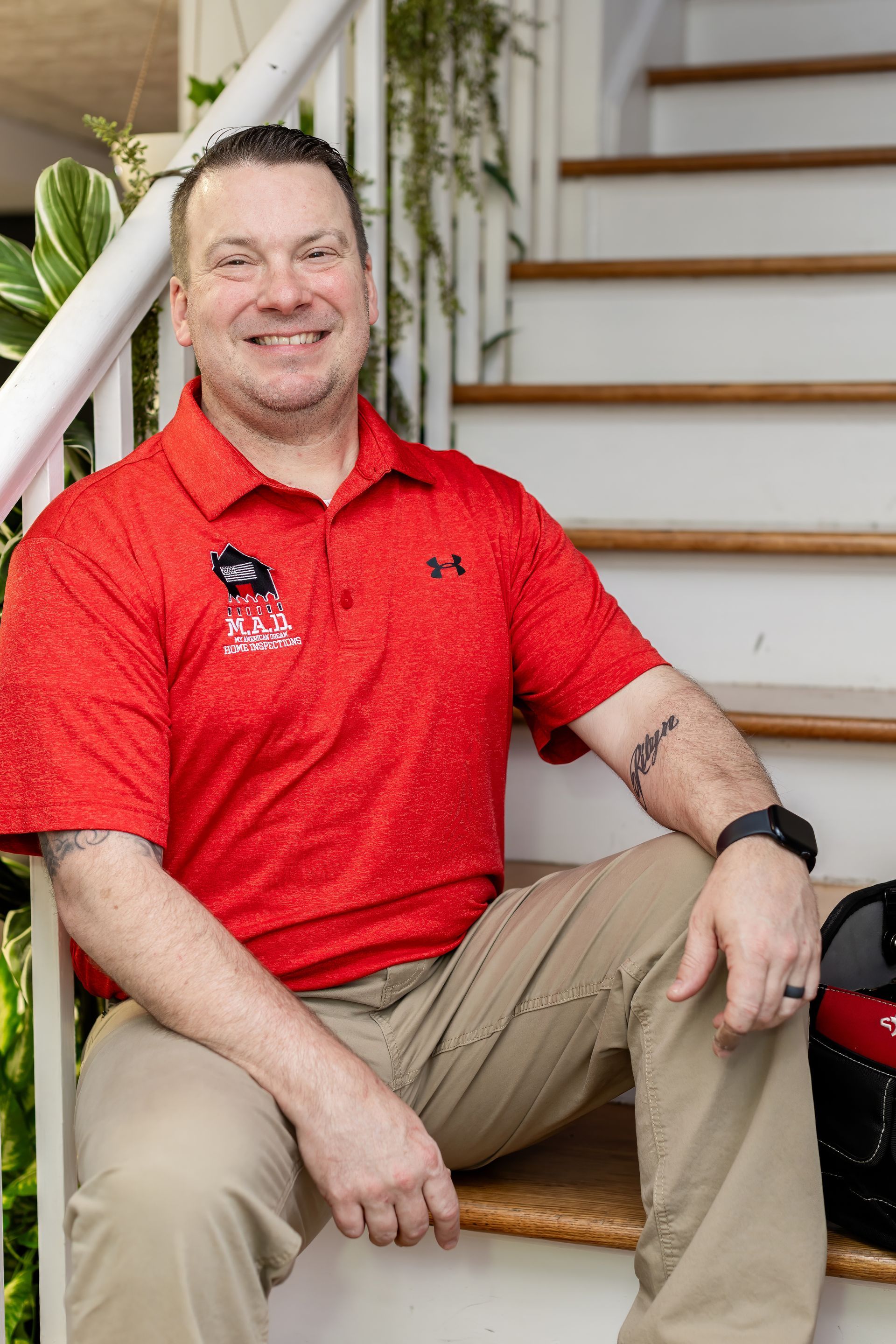 Smiling person in red polo shirt sitting on a porch step beside a white railing and staircase