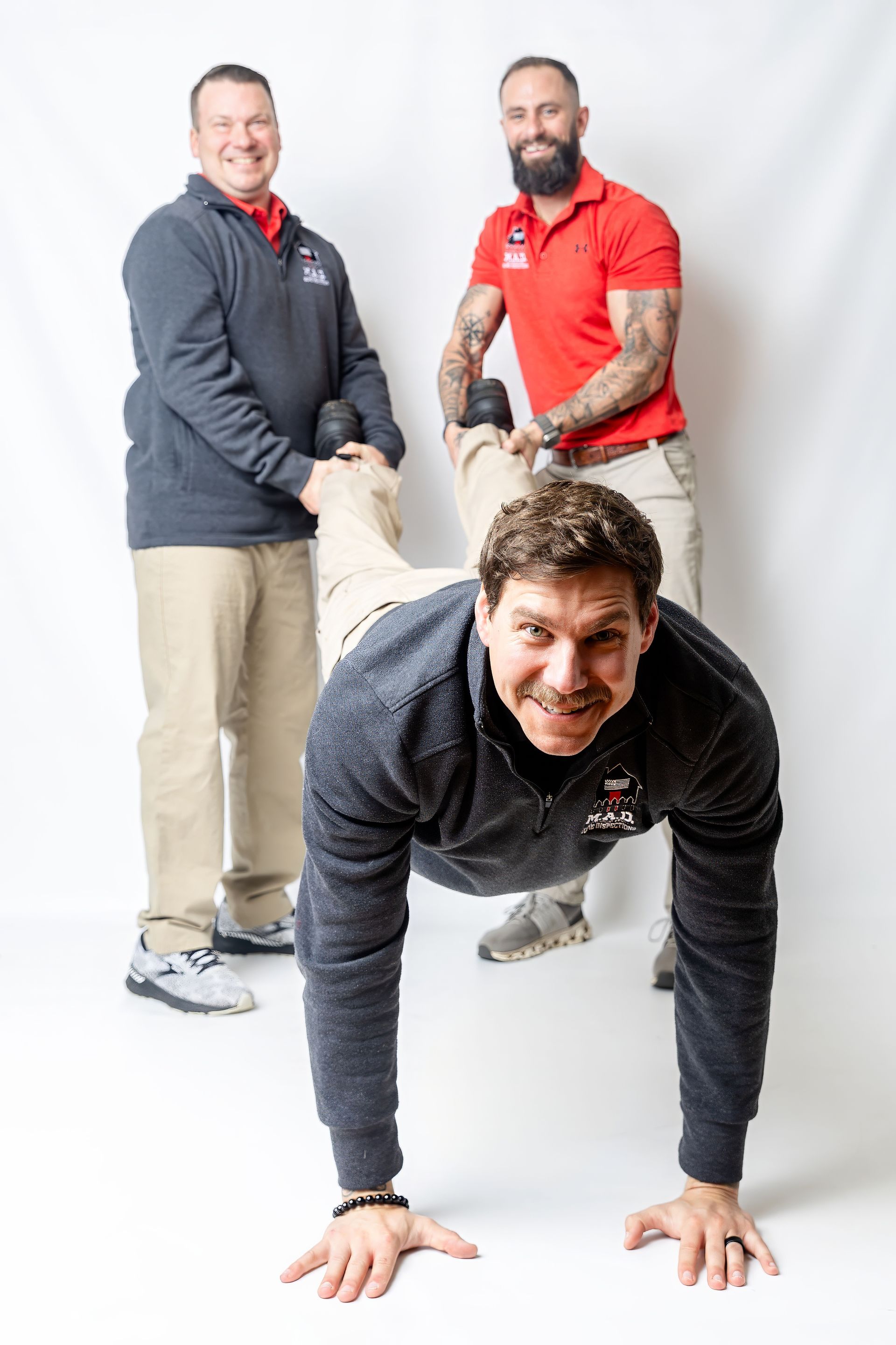 Man doing a plank while two people hold his legs in a bright studio, smiling at the camera