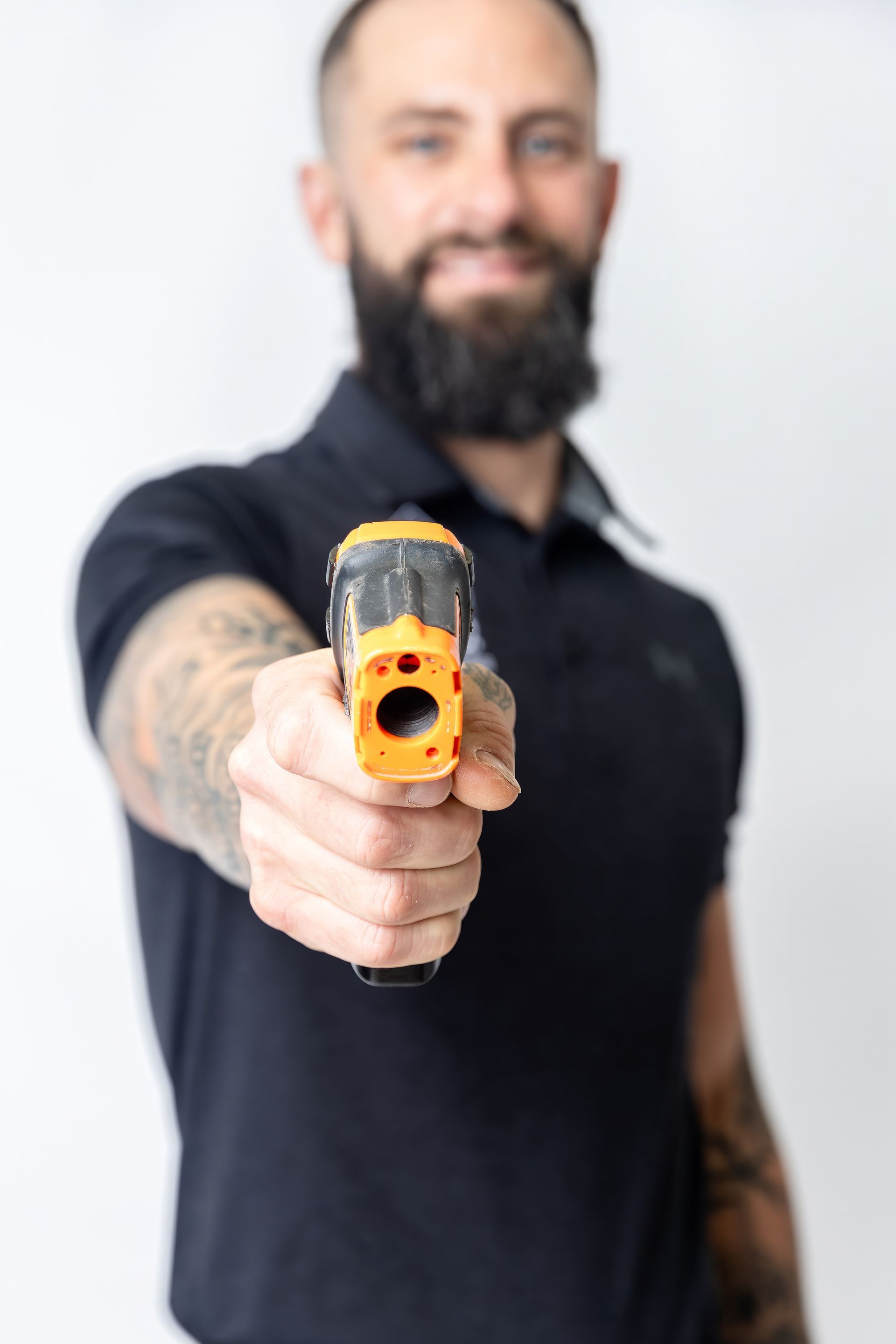 Man aiming a yellow-and-black toy gun toward the camera against a white background