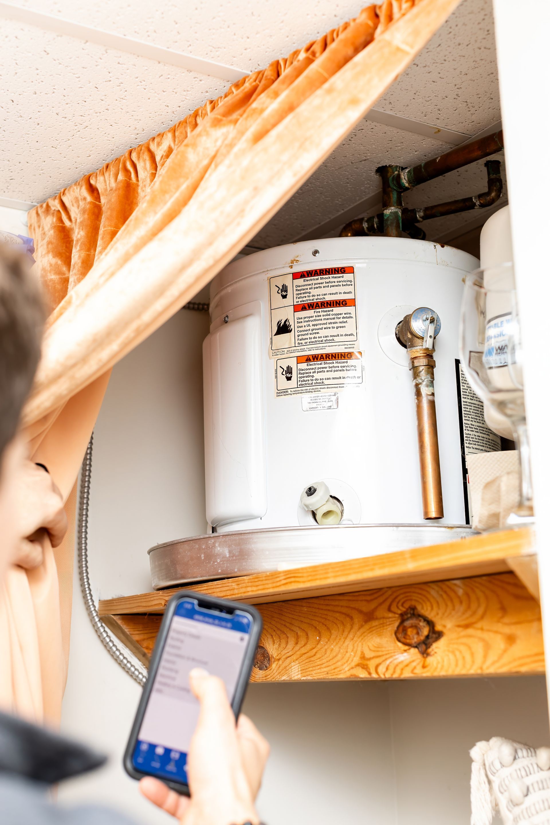 Person using a phone to inspect a white water heater in a closet-like utility space