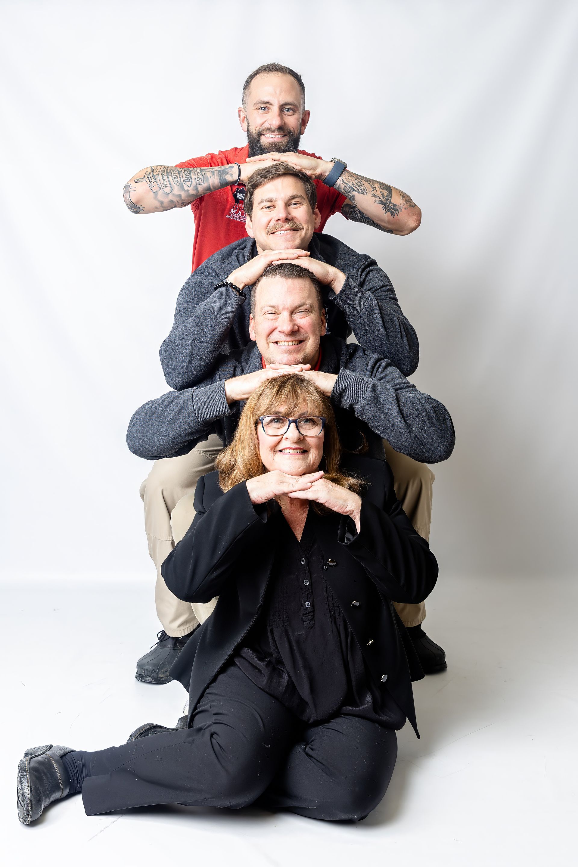 Four people stacked vertically in a playful pose against a white backdrop, smiling at the camera.