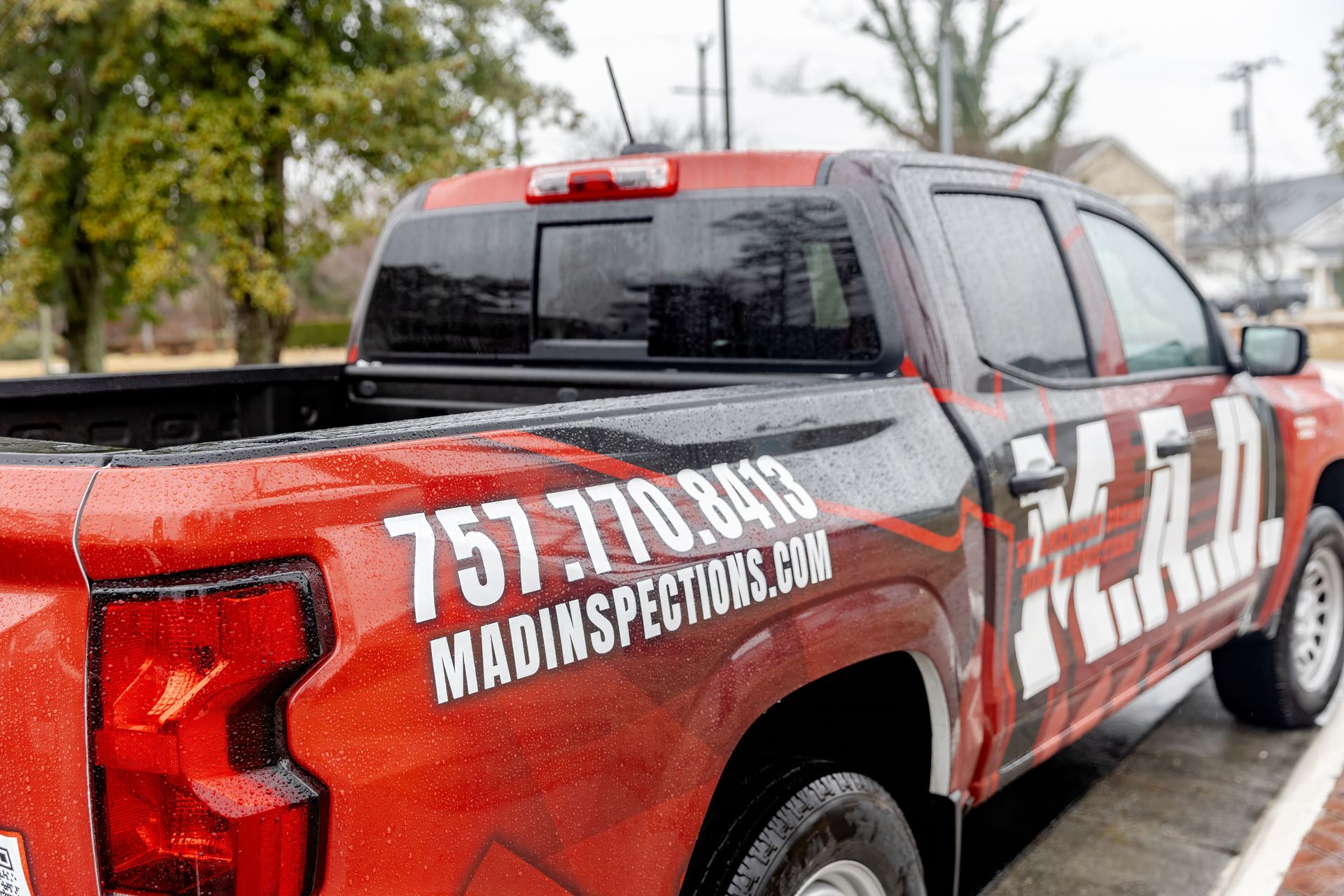 Red and black service truck with white lettering parked in a lot on a rainy day
