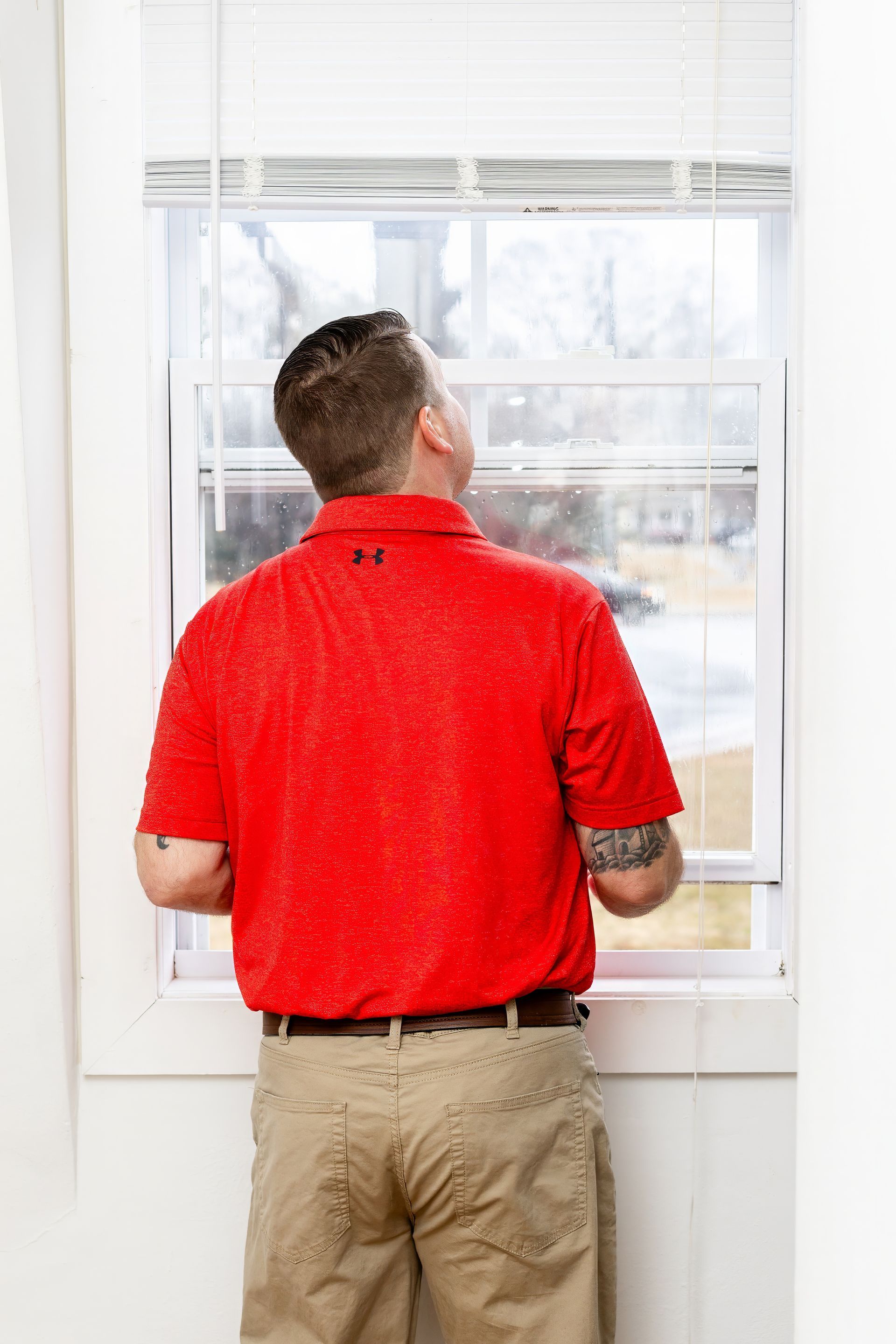 Man in red shirt standing at a window, looking outside