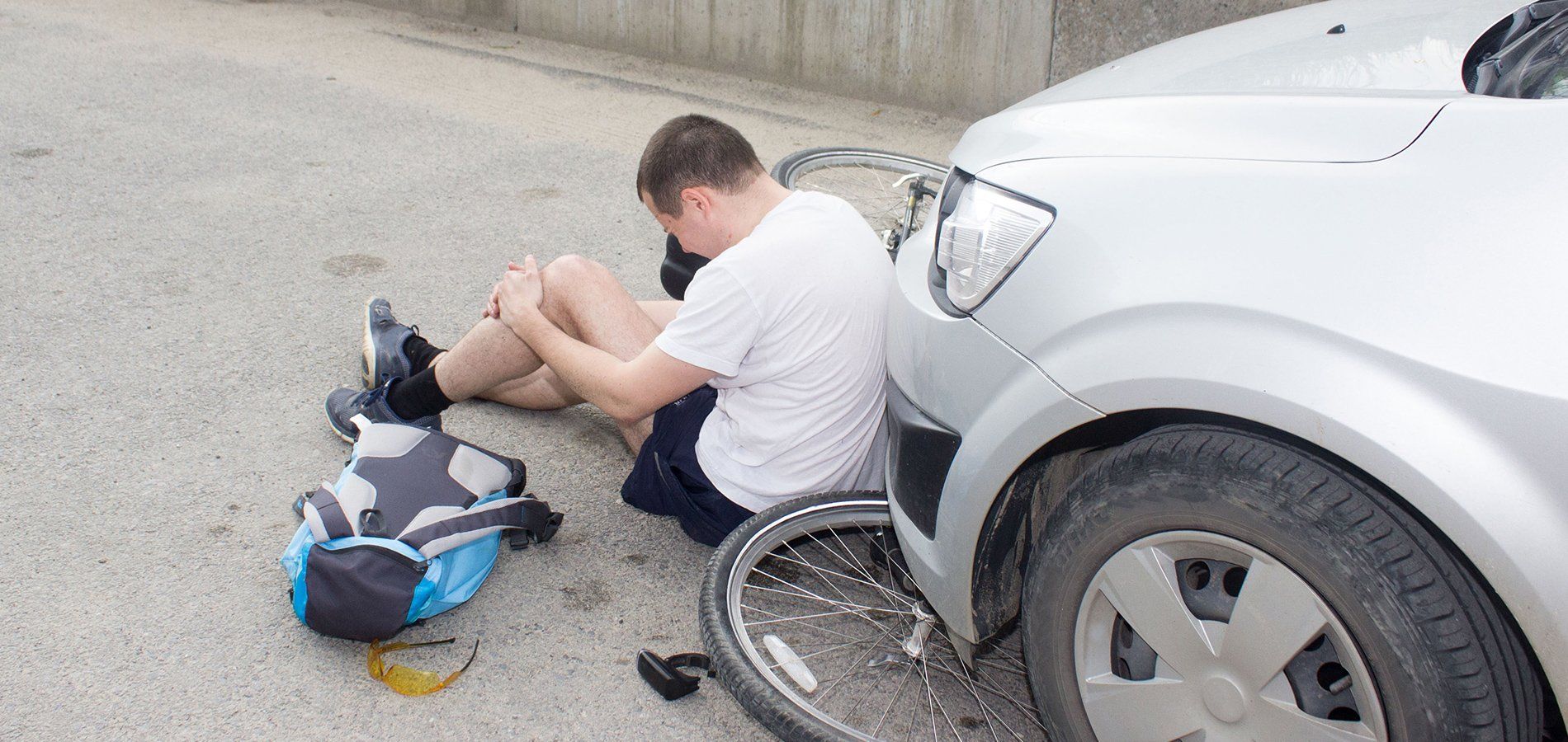 Injured bicyclist sitting on the pavement holding his knee