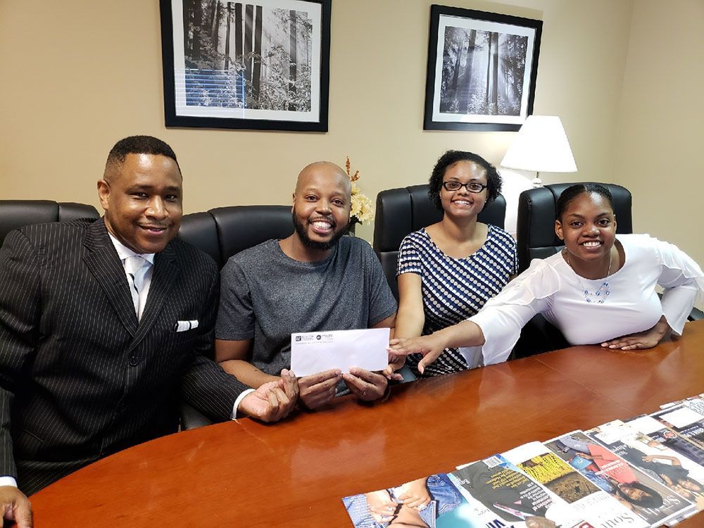 A group of happy people are sitting around a table holding a check