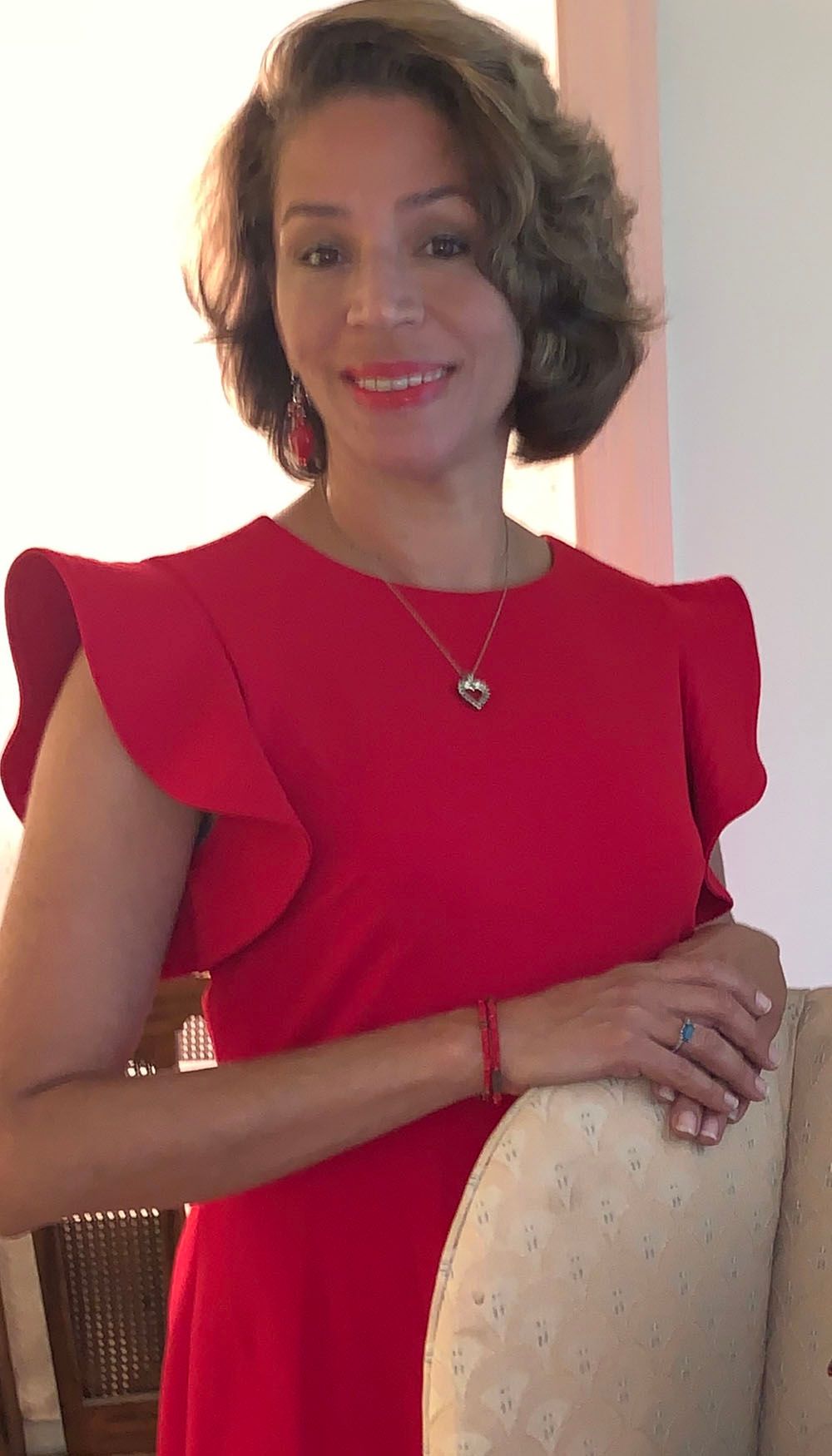 A woman in a red dress is leaning on a chair and smiling