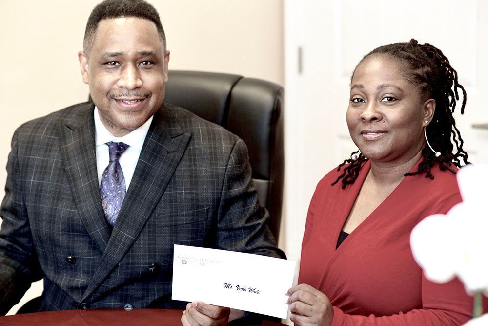 Brian D. Poe, Esq. and a woman in a red dress are sitting at a table holding a check