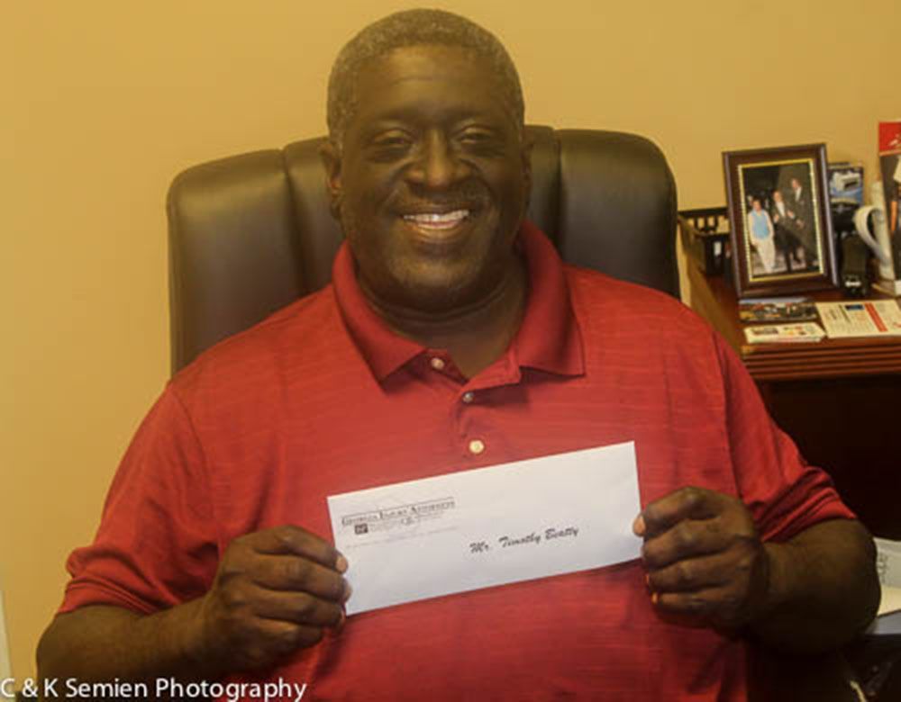 A man in a red shirt is smiling while holding a check