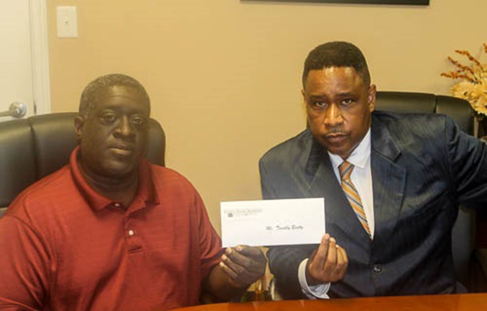 Brian D. Poe, Esq. and a man in red shirt are sitting at a table holding a check