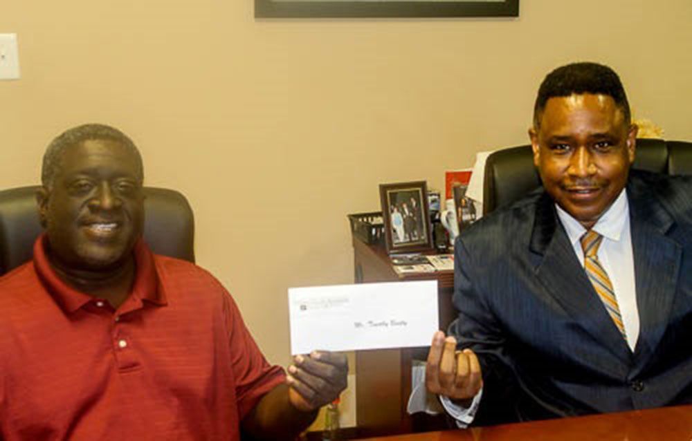 Two men are sitting at a desk holding a check