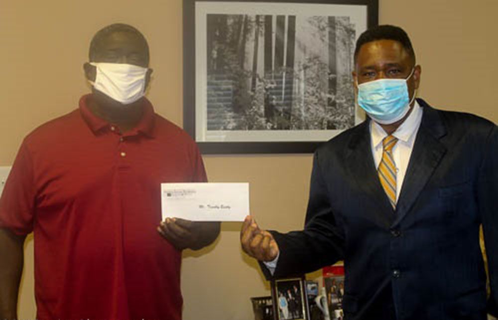 Two men wearing face masks are standing next to each other holding a check