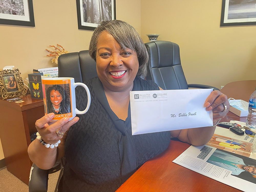 A woman is sitting at a desk holding a mug and an envelope