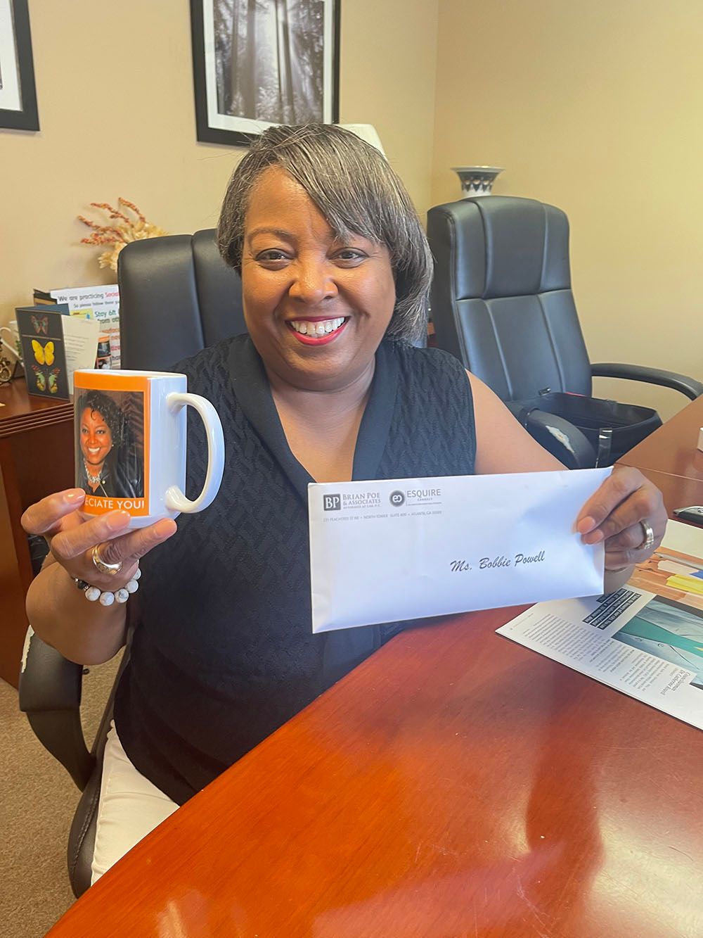 A happy woman is sitting at a desk holding a mug and an envelope