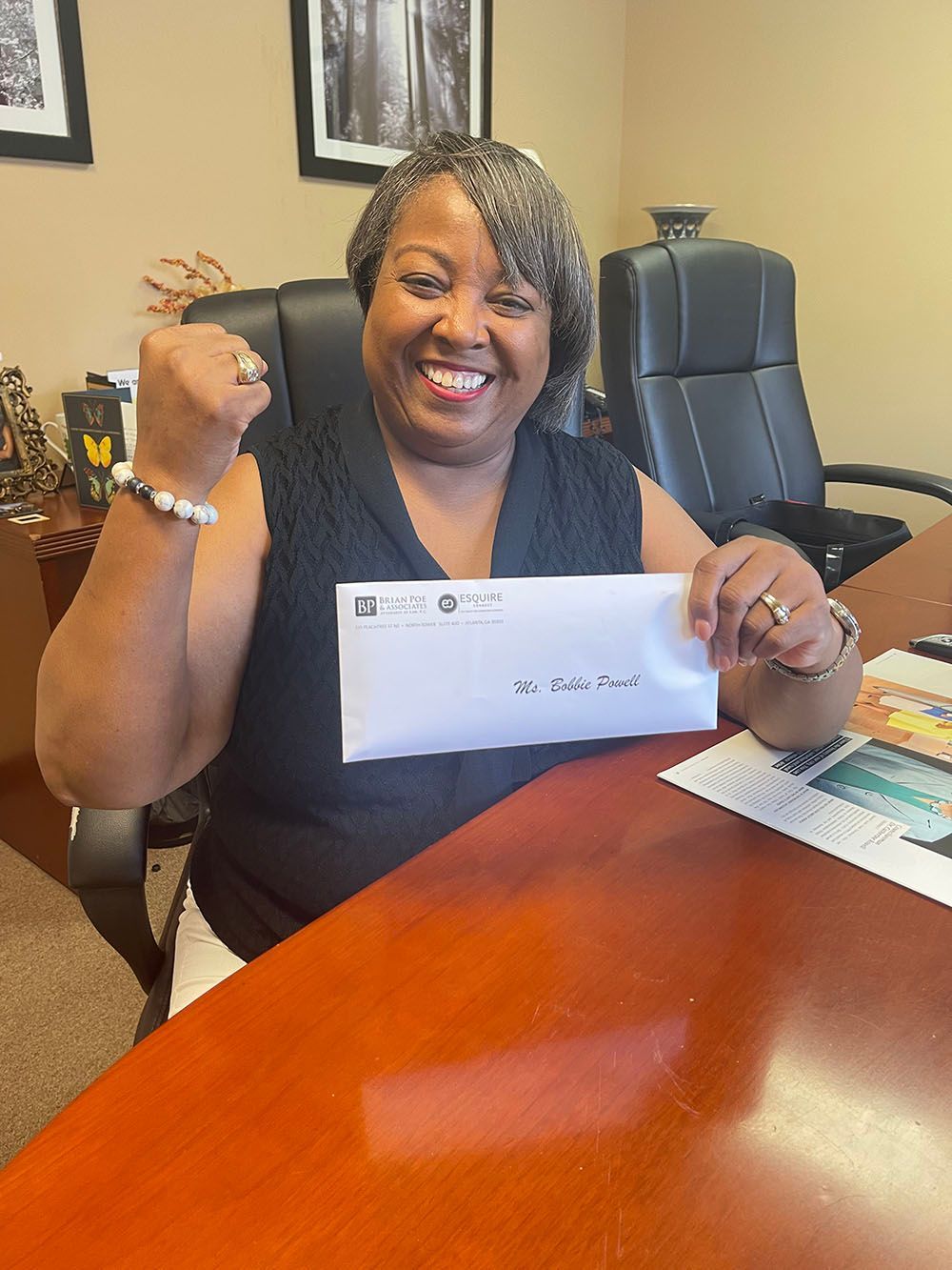 A woman wearing black is sitting at a desk holding a check