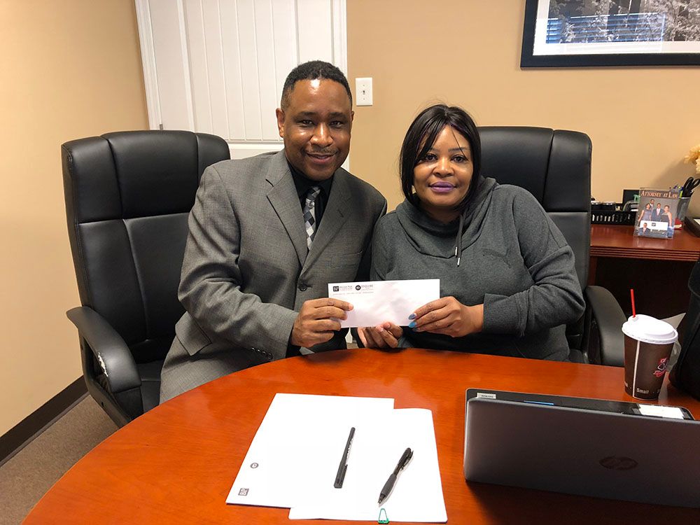 Brian D. Poe, Esq. and a woman in long sleeves are sitting at a table holding a check