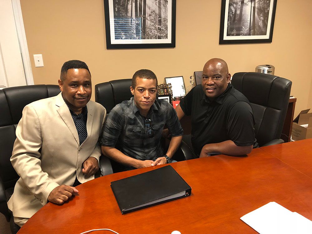 Three men are sitting at a table with a laptop on it