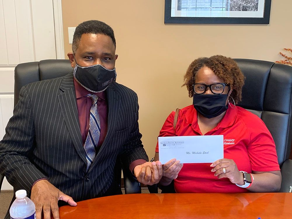 Brian D. Poe, Esq. and his client wearing masks are sitting at a table holding a check