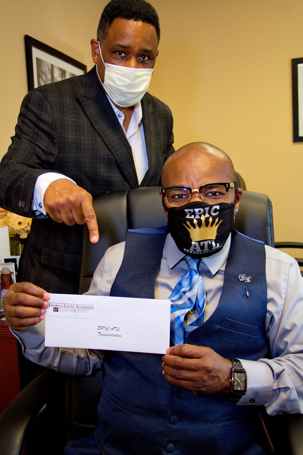 Brian D. Poe, Esq., and his client wearing masks are sitting at a table showing a check
