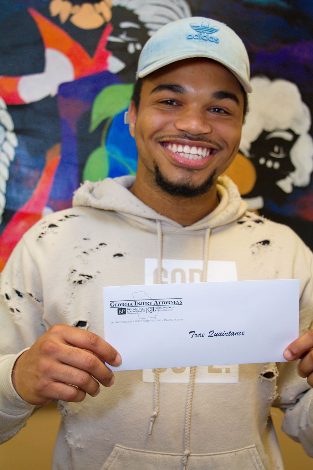 A man wearing a hat is smiling while holding a check