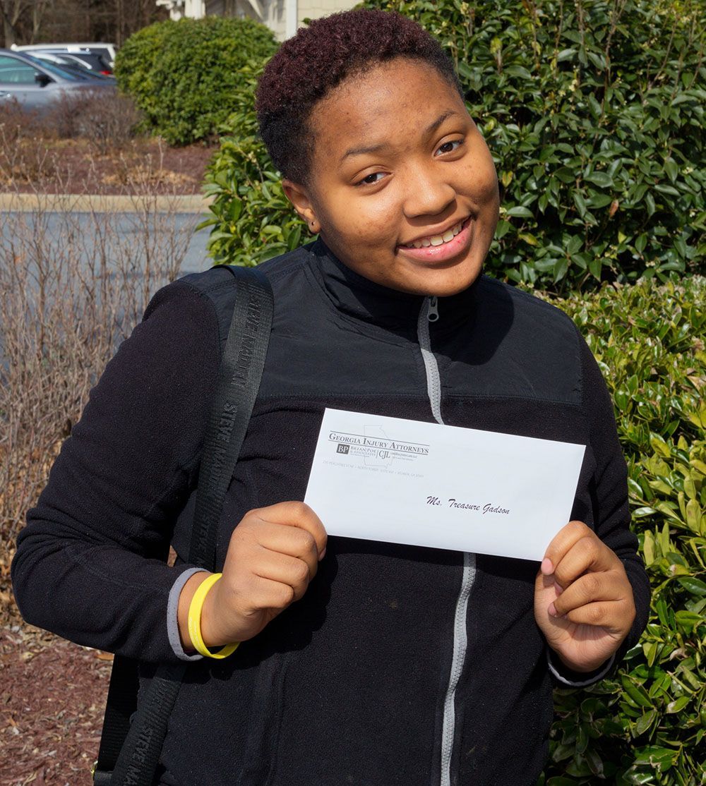 A woman in a black jacket is smiling while holding an envelope