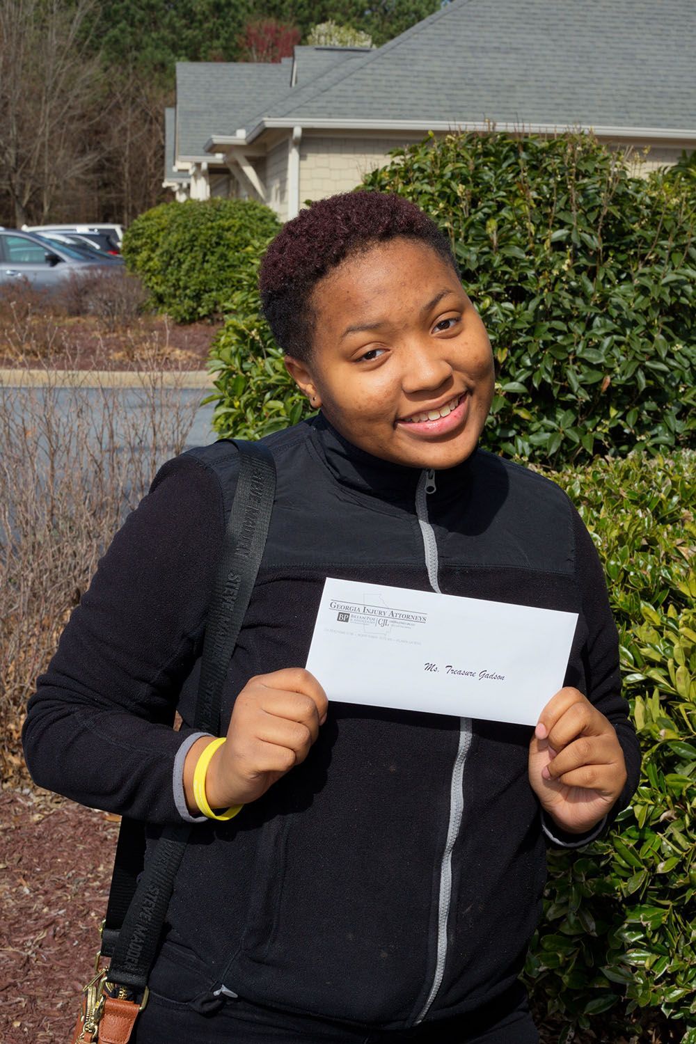 A smiling woman in a black jacket is holding a chek