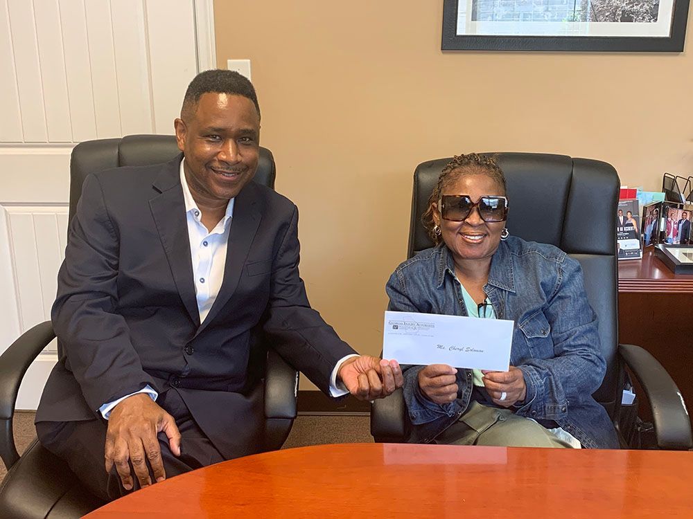 Brian D. Poe, Esq. and a woman in a denim jacket are sitting at a table holding a check