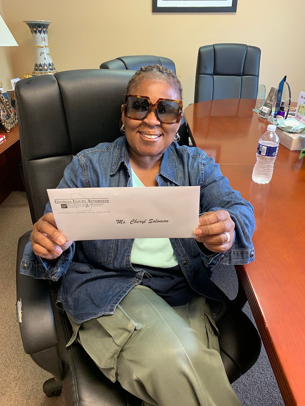 A woman in a denim jacket is sitting in a chair holding a check