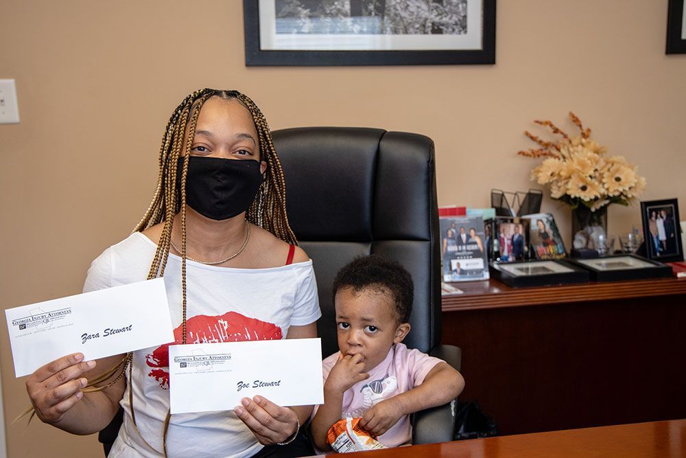 A woman wearing a mask and a child are sitting at a table holding envelopes