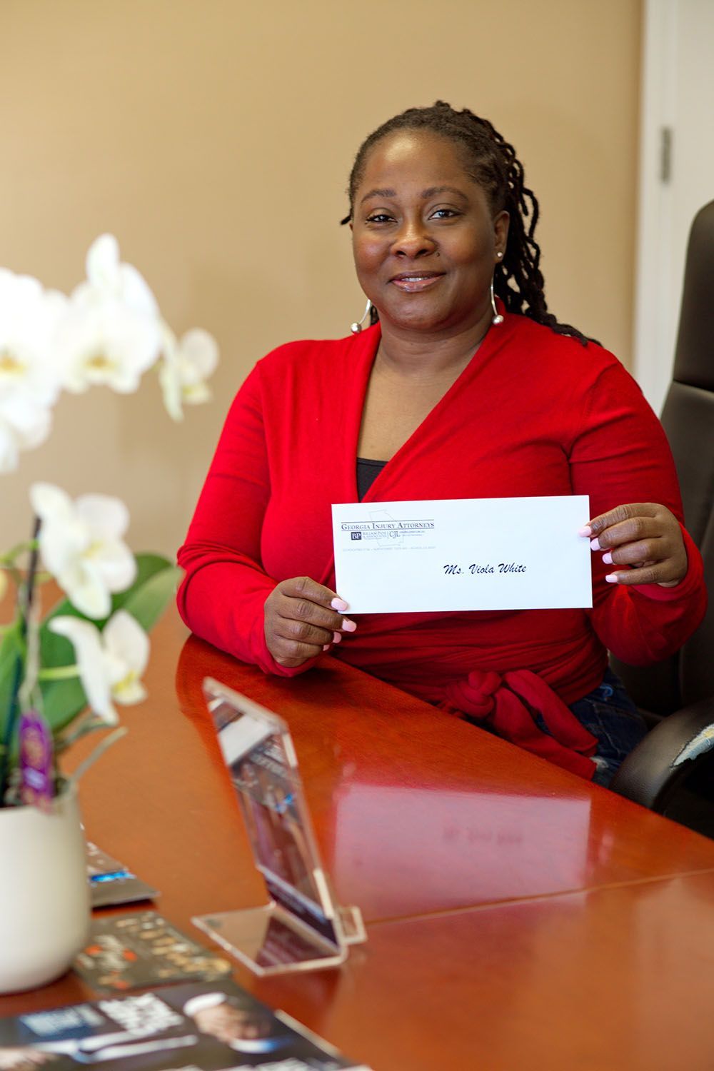 A smiling woman in a red dress is sitting at a table holding a check