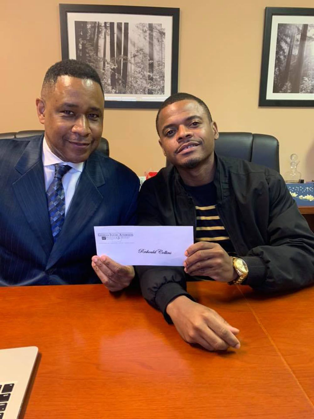 Two men are sitting at a desk holding a check.
