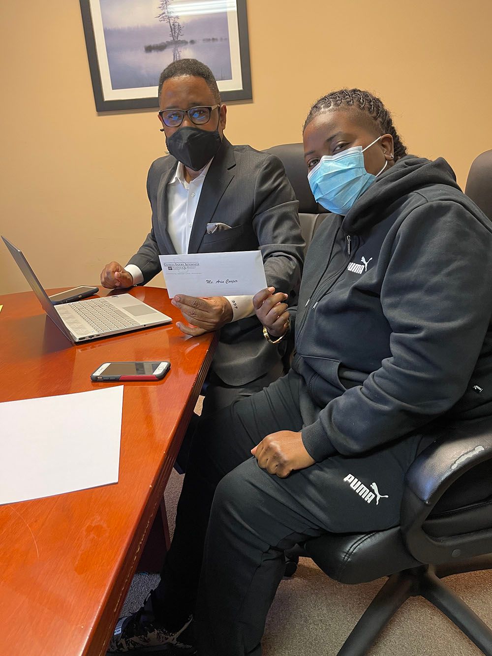 Brian D. Poe, Esq. and a woman wearing masks are sitting at a table with a laptop
