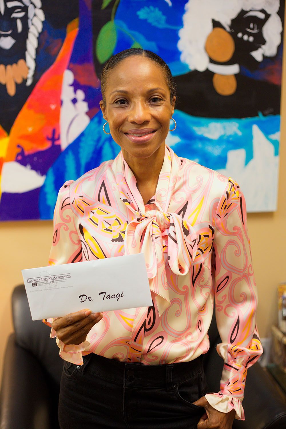 A happy client in a pink shirt is holding a check in front of a painting